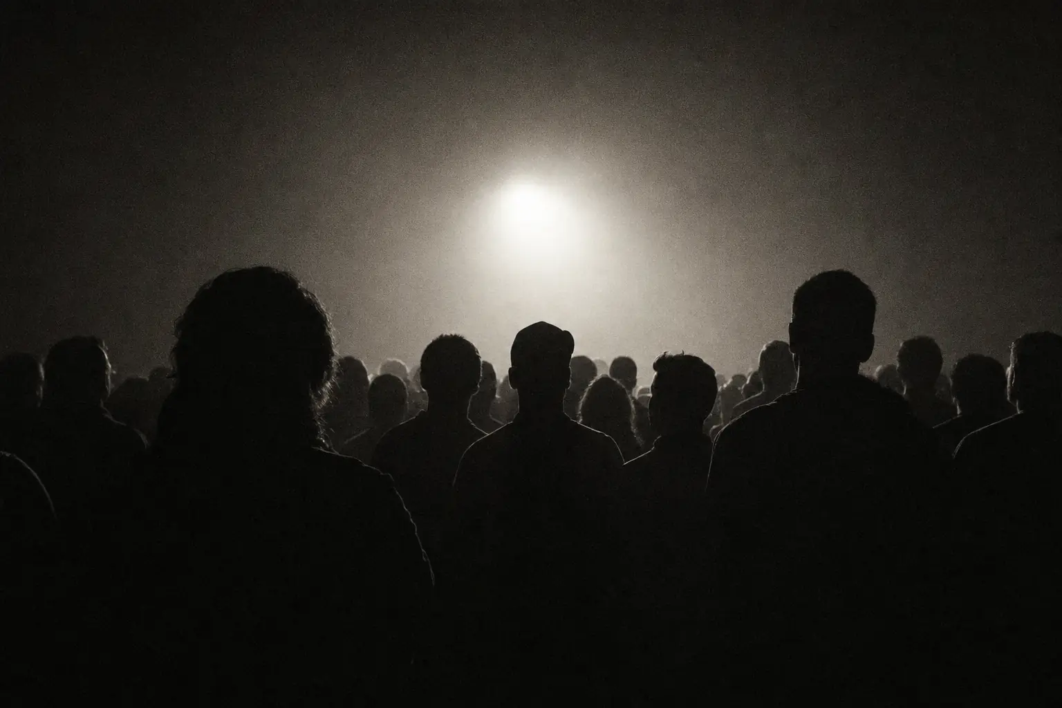 Anonymous crowd in silhouette, backlit inside a dark room.